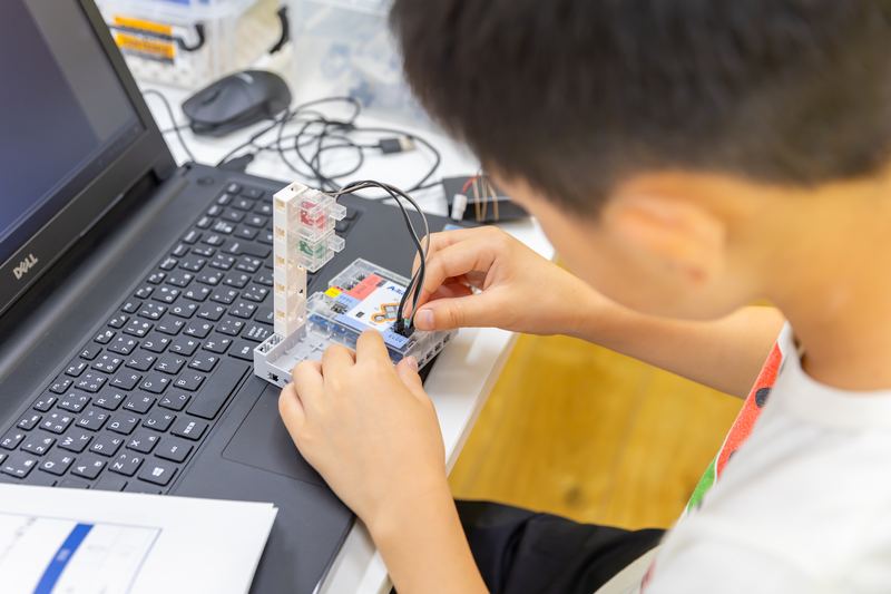 ロボットの配線とパソコンを確認しながら作業する小学生